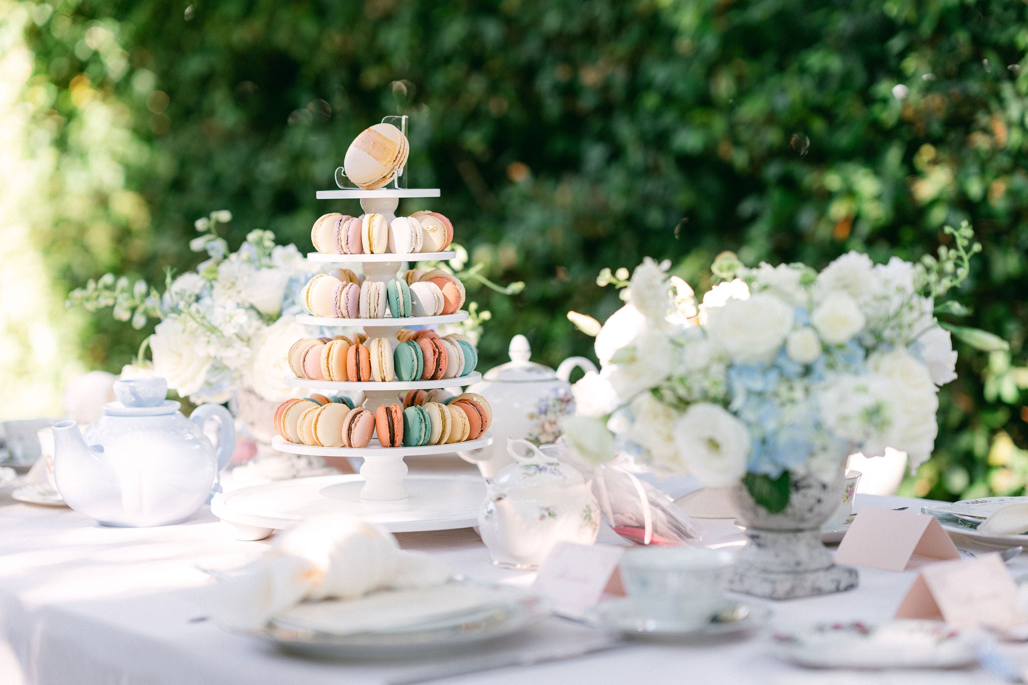 Macaron tower on a table with floral arrangements and teacups outdoors
