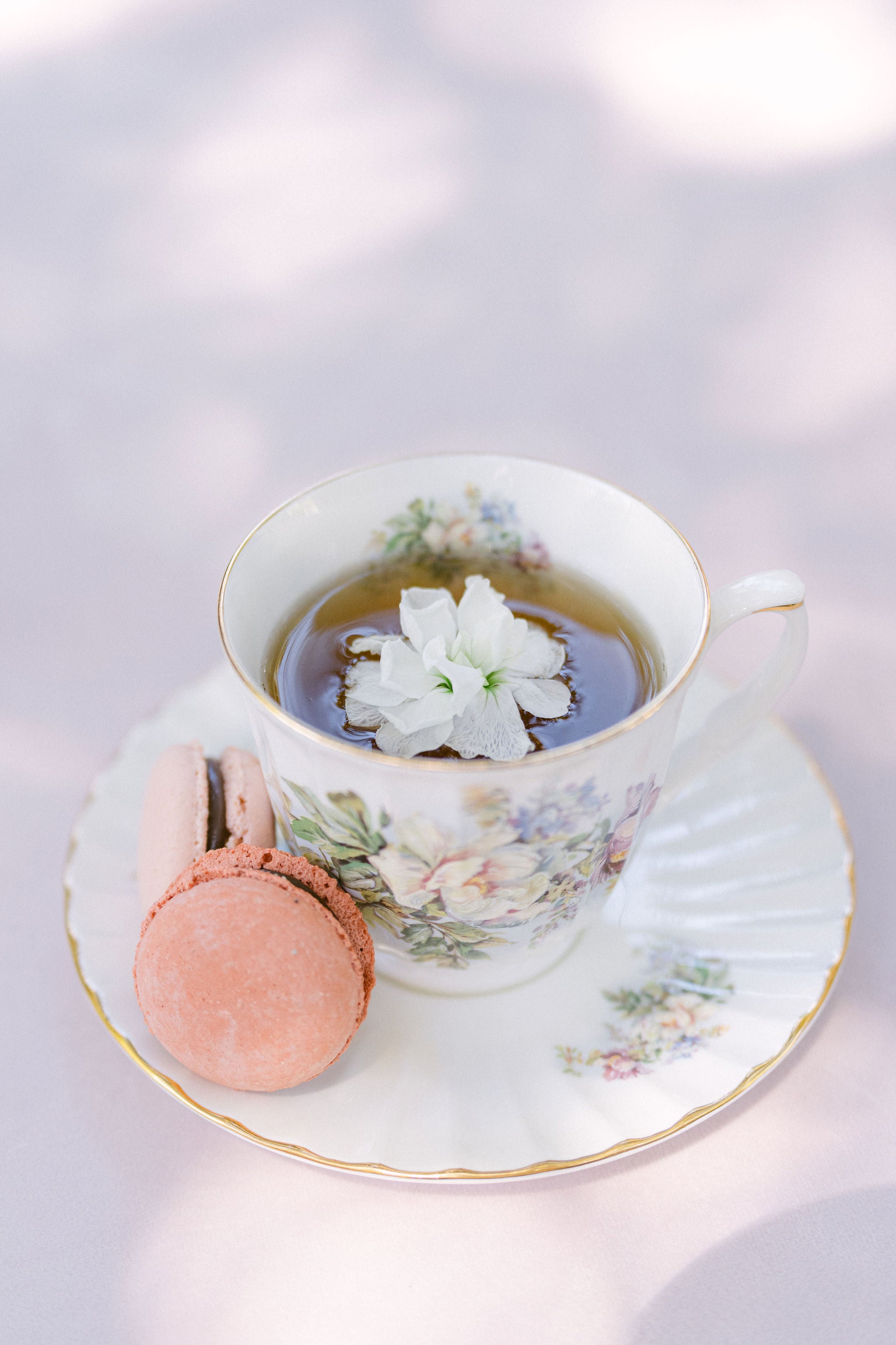 Teacup with floral design, pink macaron, and white flower on a light background