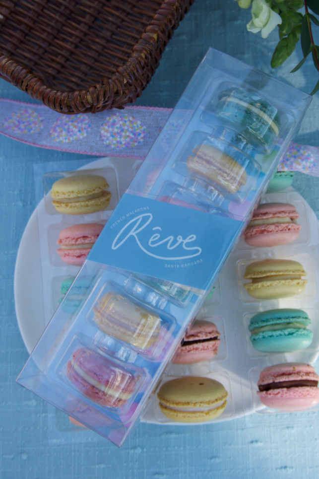 Packaged macarons with a decorative label on a blue surface with flowers.