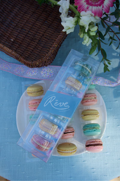 Packaged macarons with a decorative label on a blue surface with flowers.