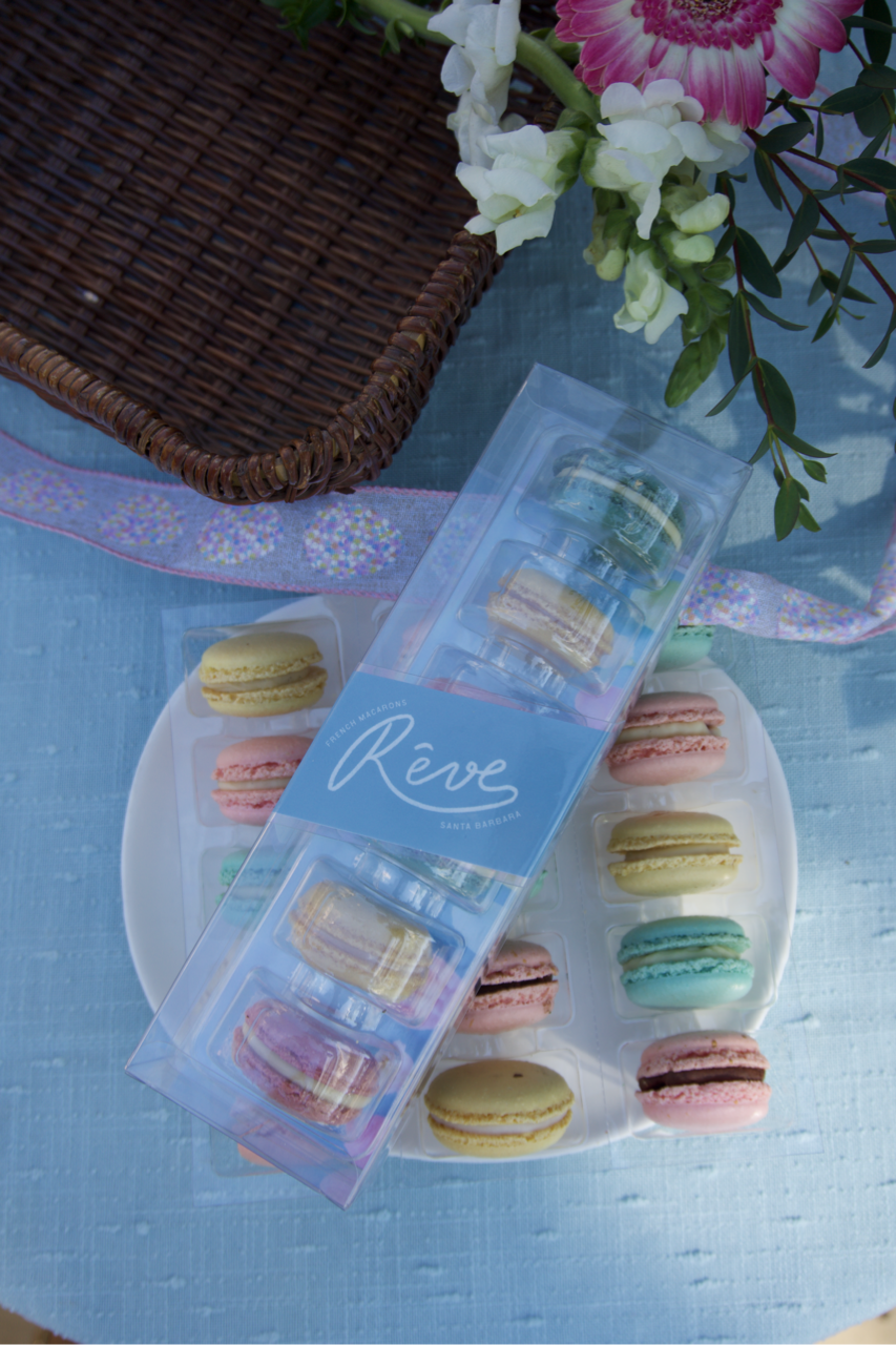 Packaged macarons with a decorative label on a blue surface with flowers.