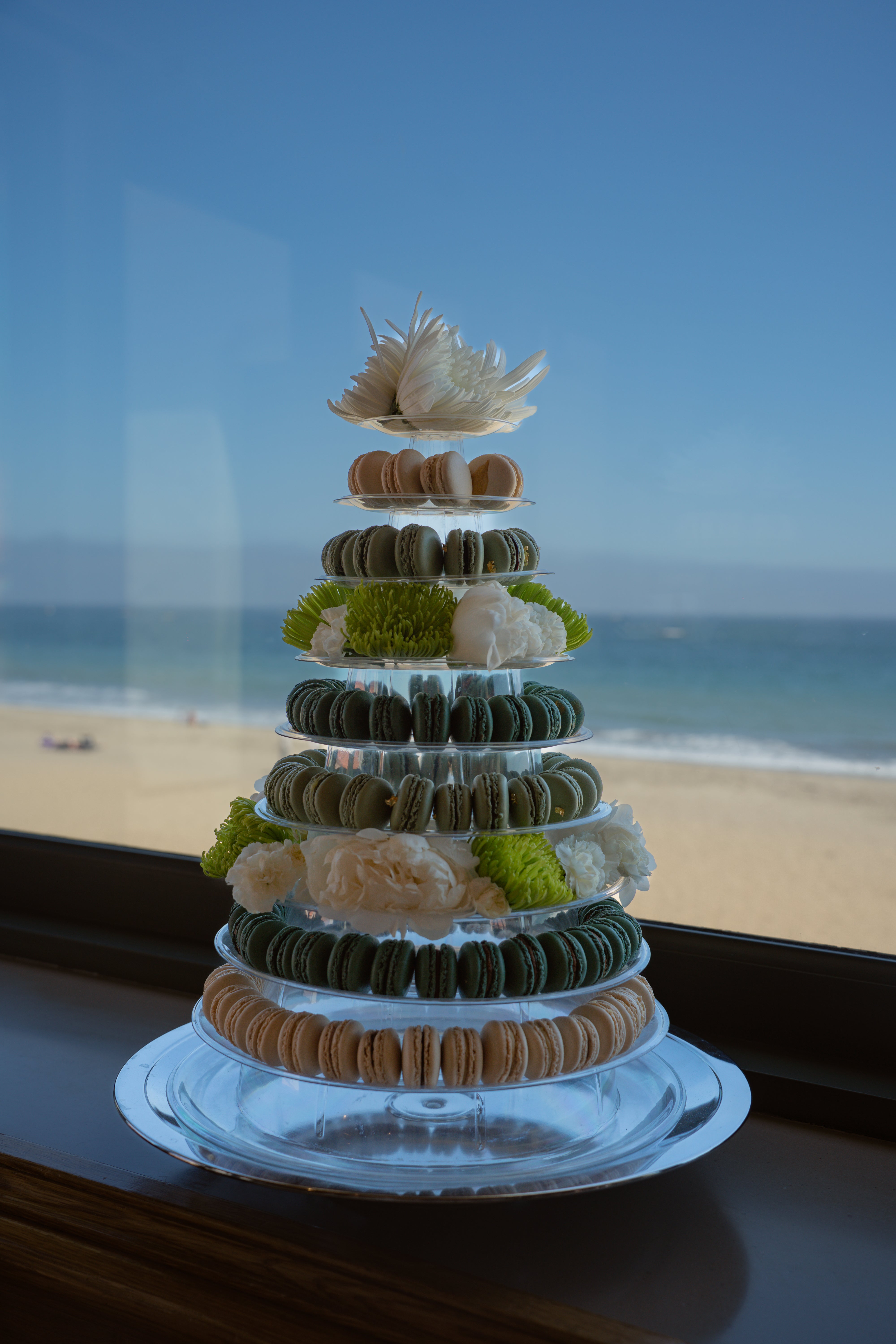 Luxury dessert Multi-tiered wedding Macaron tiered display with decorative elements on a clear stand, set against a beach backdrop in Santa Barbara SoCal