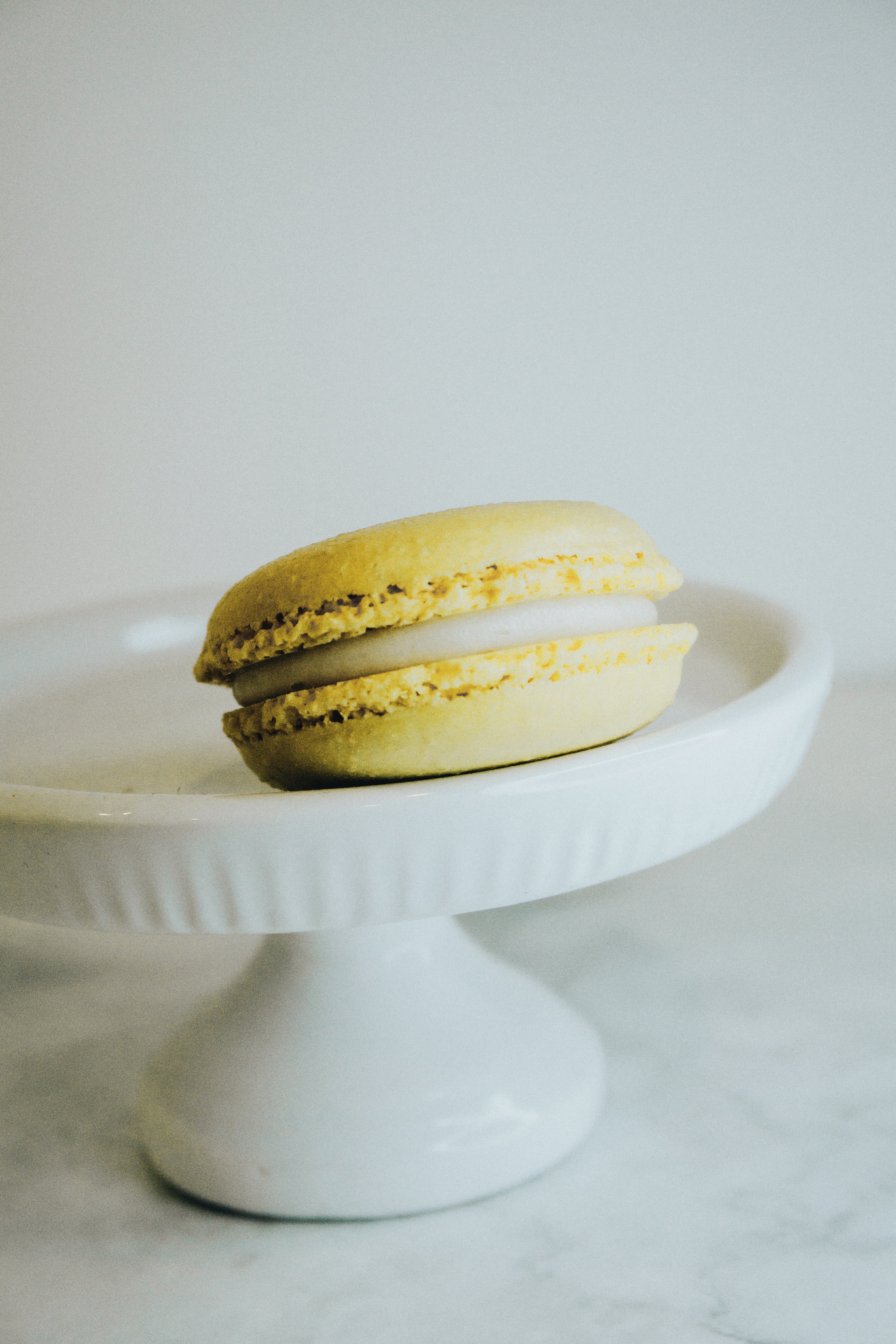 One yellow macaron on a white cake stand with a light background